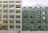 Gen Westen liegen das in portugiesische Kacheln gekleidete Gebäude von noAarchitecten und METAs Wohnhaus, dessen messingfarbene Balkone Glanz auf die Fassade bringen. 