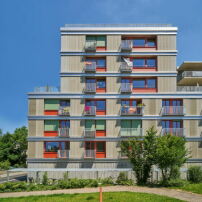 Eine Holzfassade und farbige Fensterelemente machen das äußere Erscheinungsbild des hybriden Wohn-, Arbeits- und Universitätsprojekts aus.    